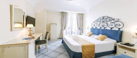 A hotel room with a bed, a desk, a chair, a nightstand, and a mirror.