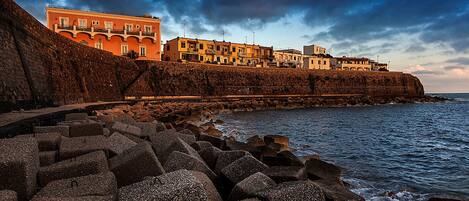 A coastal town with buildings along the cliffside, a rocky breakwater, and the sea.