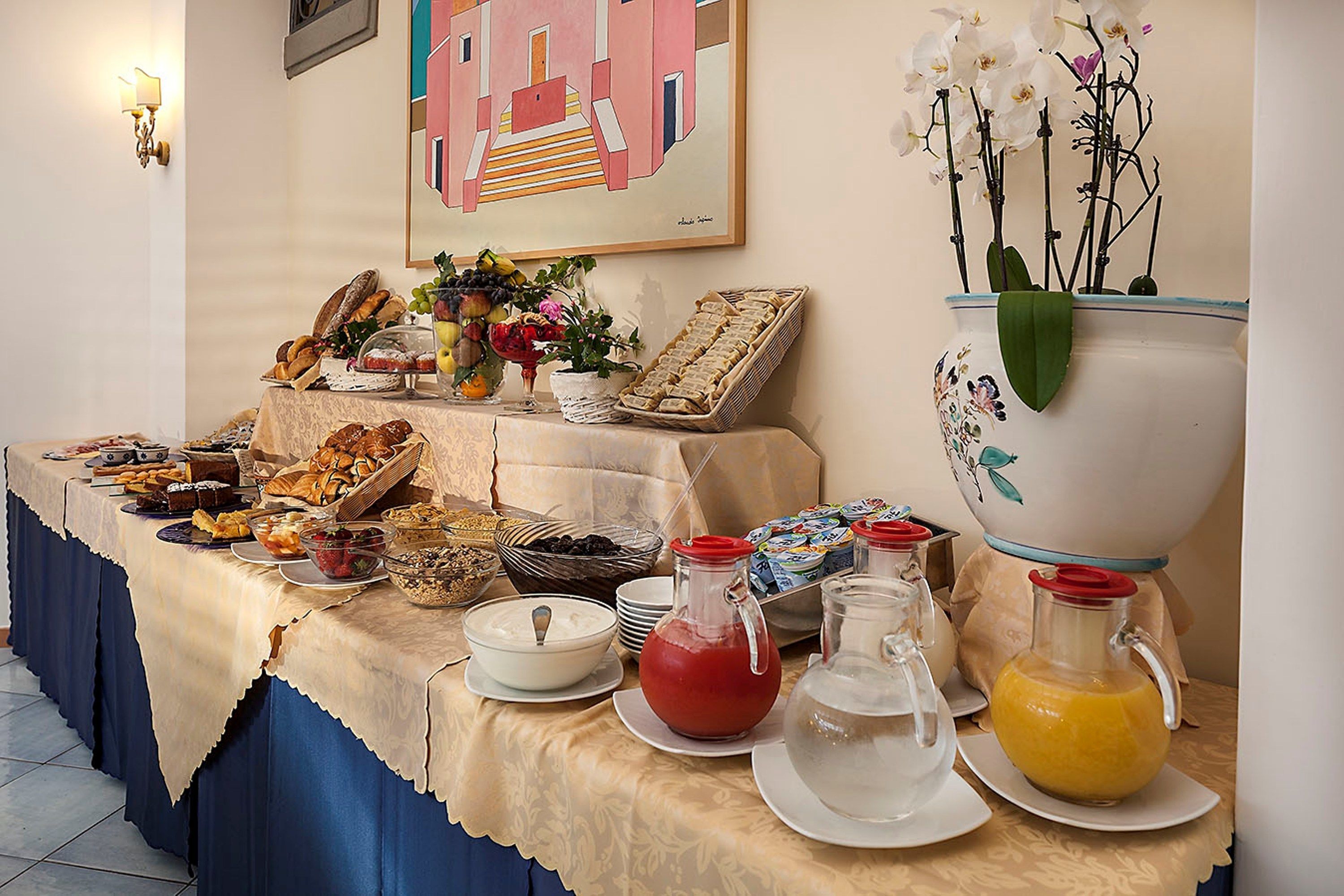 A buffet table with various food items, a decorative vase with flowers, and a painting on the wall.