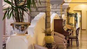 A lobby with a stone column, a large decorative vase, wicker chairs, and a piano. - Hotel Nettuno (Forio)