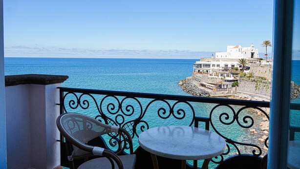A balcony with two chairs and a table, overlooking a coastal town with buildings and the sea. - Hotel Nettuno (Forio)