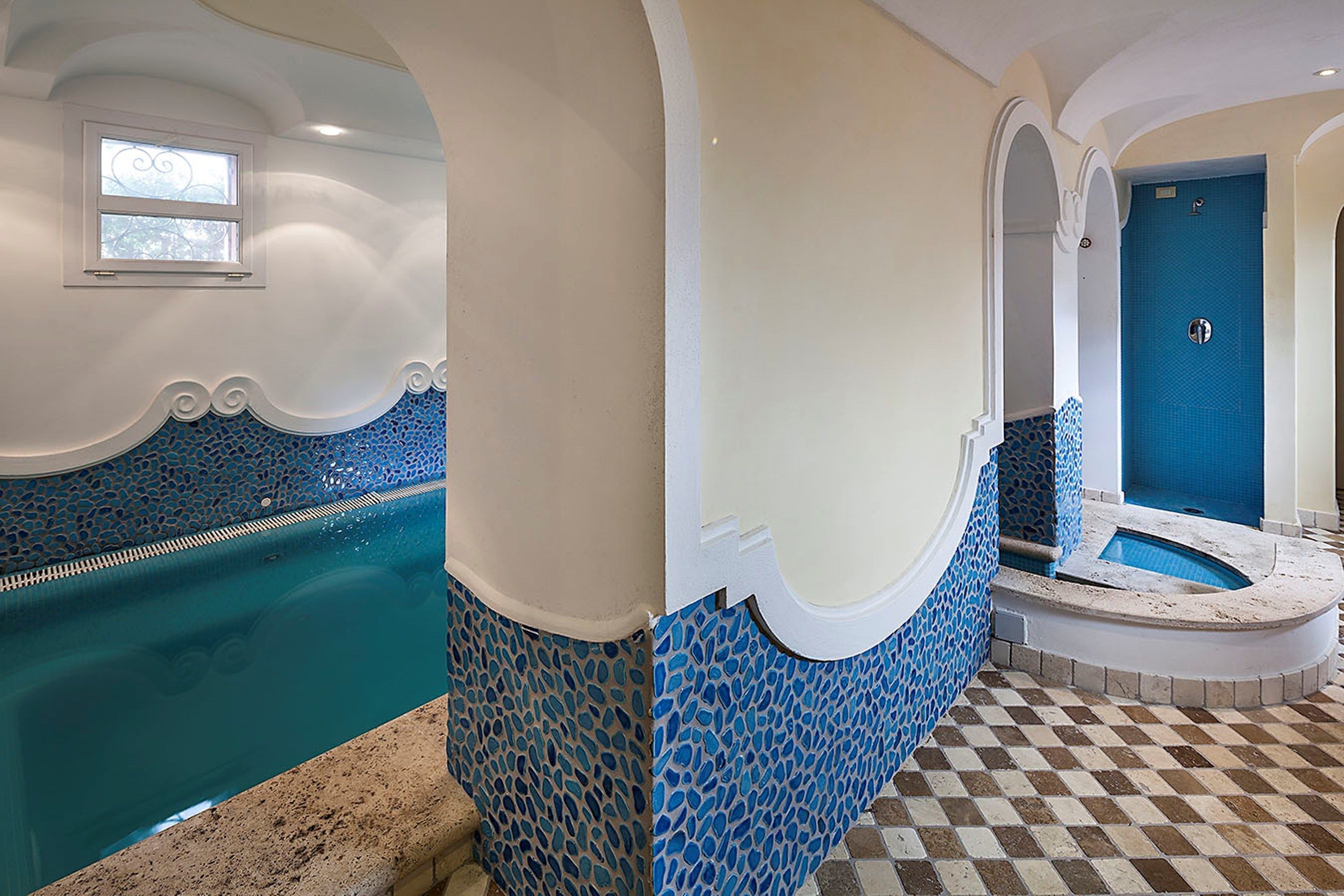 Una piscina con piastrelle blu a mosaico, pavimento a scacchi e una porta blu.