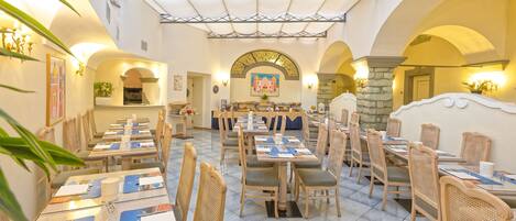A spacious dining area with multiple tables and chairs, a high ceiling with a patterned design, and a central archway.