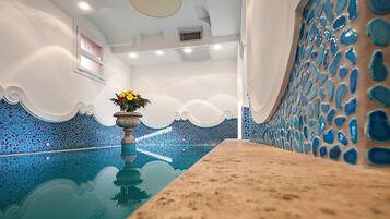 Una piscina con mosaicos azules, un florero y un techo con iluminación empotrada.