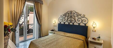 A bedroom with a large bed, a chandelier, a nightstand, and a view of the outside.