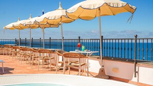 A poolside area with lounge chairs, umbrellas, and a view of the sea. - Hotel Nettuno (Forio)