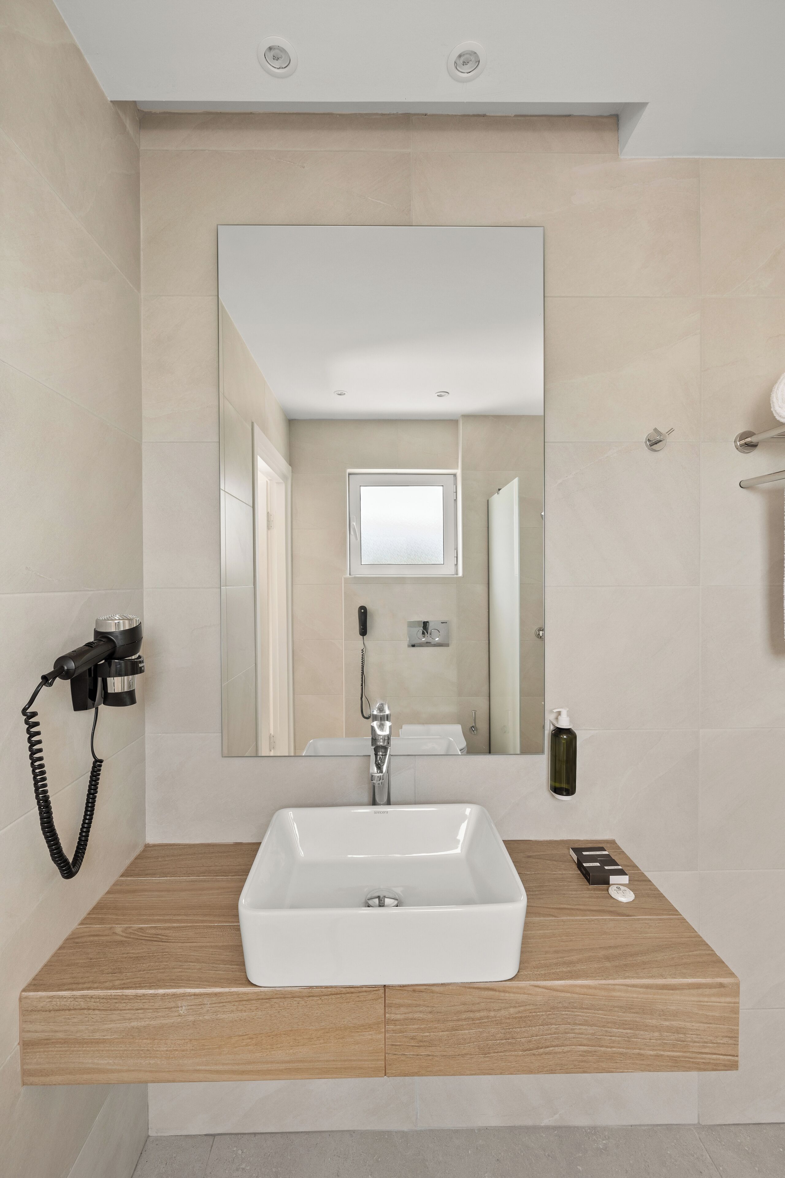 A modern bathroom with a large mirror, a white sink, and a wooden vanity.