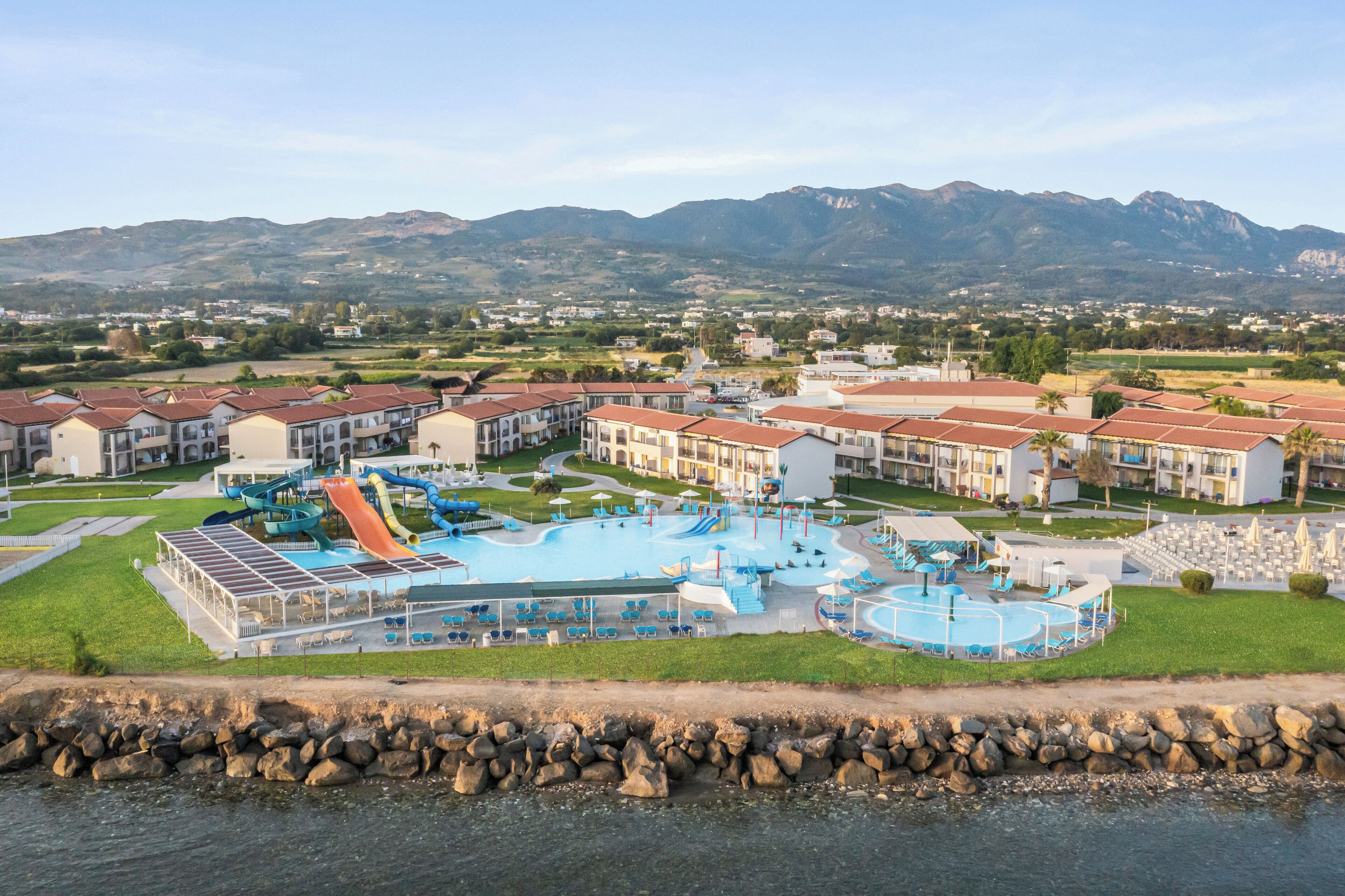 A resort with a large swimming pool, multiple slides, and a view of mountains in the background.