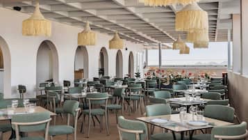 Un restaurante con sillas y mesas tapizadas de verde, lámparas colgantes tejidas y vistas al mar.