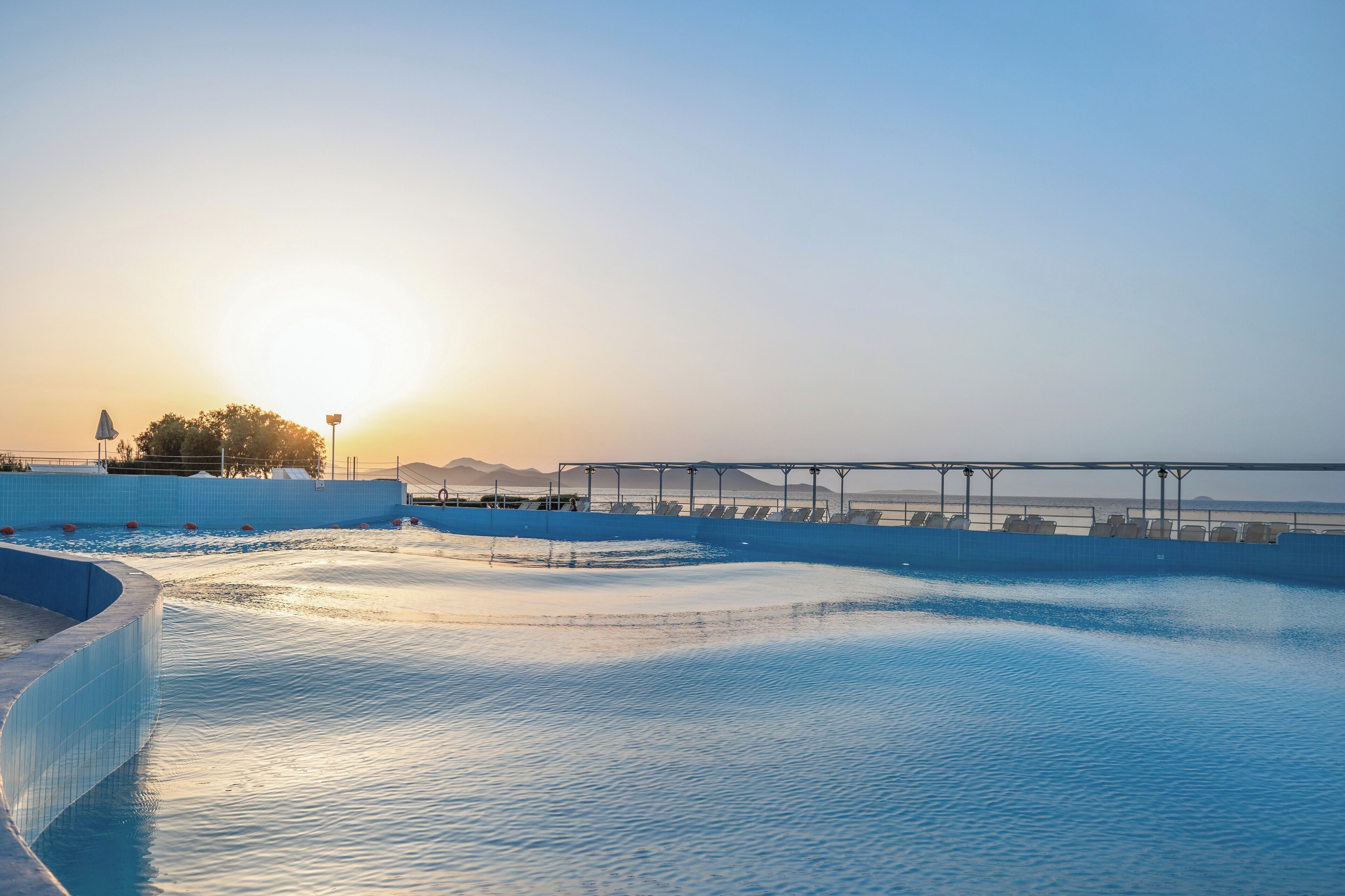 A swimming pool with a clear view of the sunset and distant mountains.