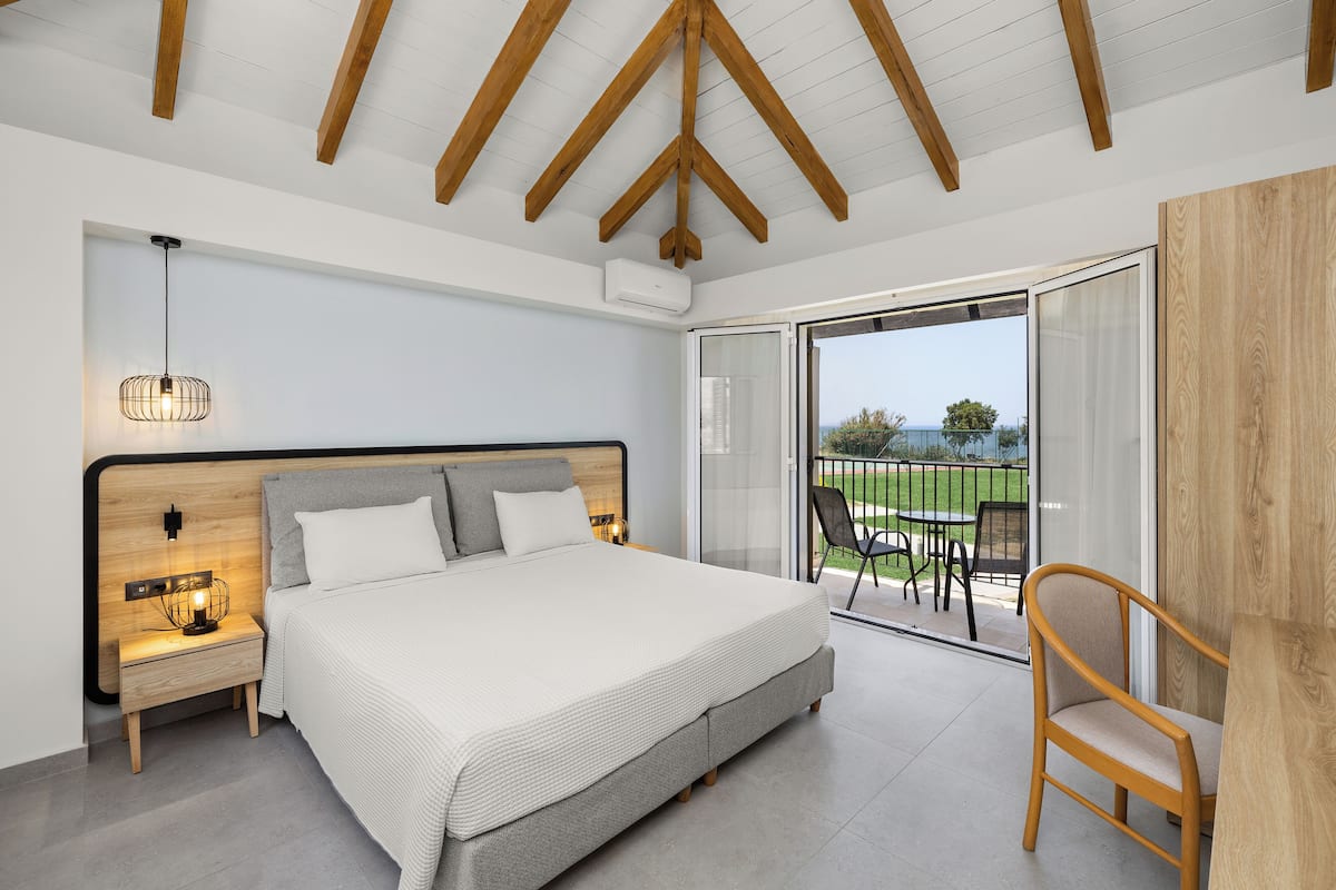 A bedroom with a large bed, wooden headboard, bedside table with lamp, and a view of the outdoors through a sliding glass door.