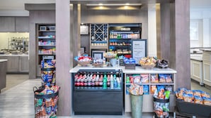 Una tienda llamada 'The Shop' con estantes llenos de refrigerios, una sección refrigerada y una exhibición de productos locales.