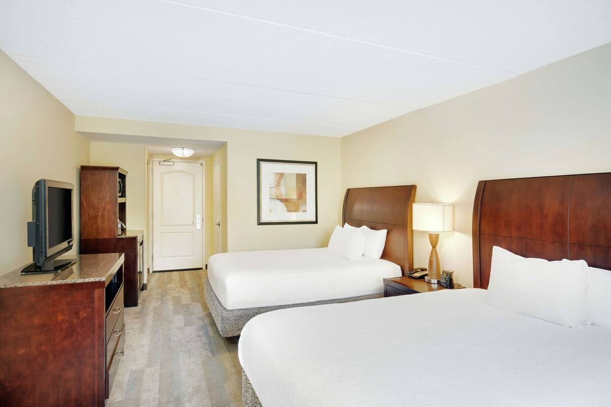 Een hotelkamer met twee bedden, een televisie, een bureau en een ingelijst schilderij aan de muur.