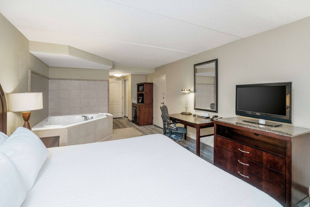 Hotelkamer met een groot bed, een bureau, een televisie, een bureaulamp, een stoel, een badkamer met bad en een spiegel.