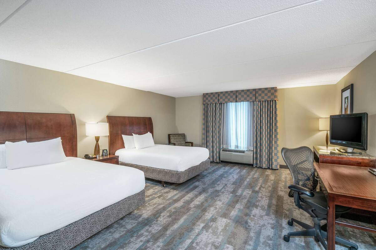 Hotelkamer met twee bedden, een bureau, een stoel, een televisie en een raam met gordijnen.