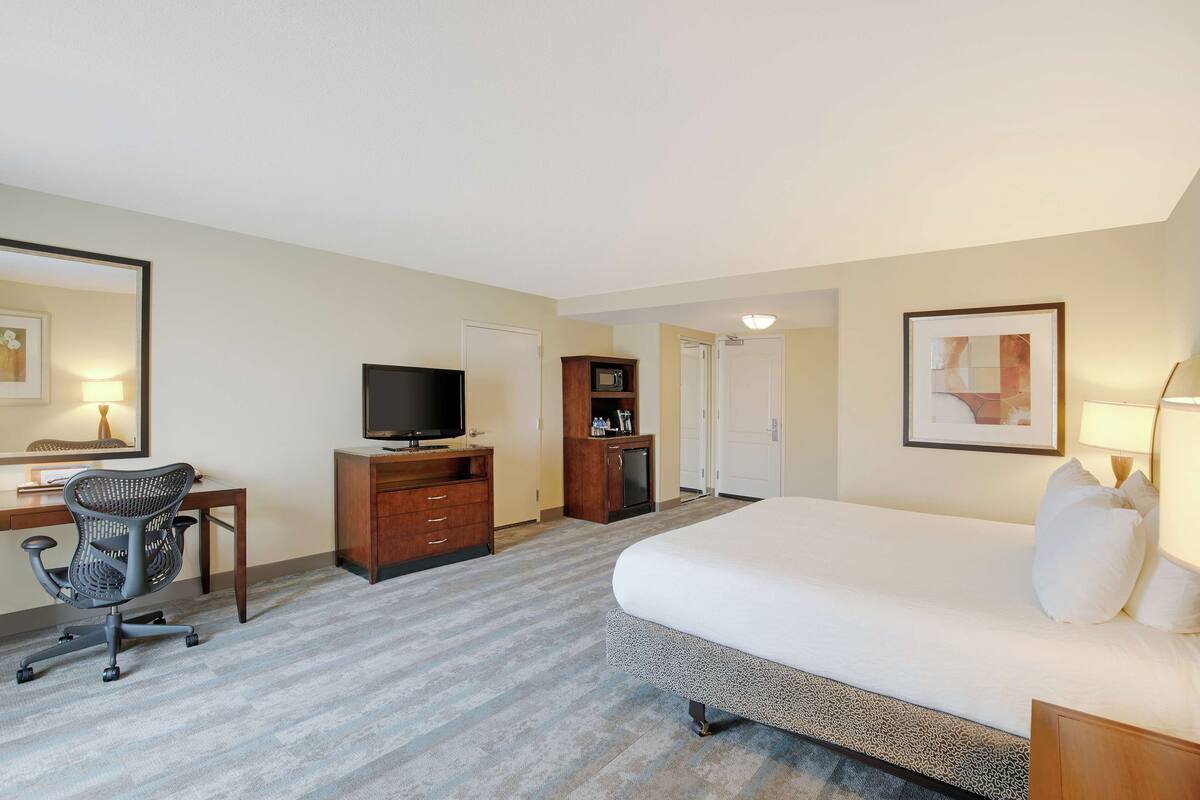 Hotelkamer met een bed, bureau met een computer, stoel, televisie, magnetron en een deur.