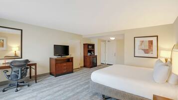 Habitación de hotel con cama, escritorio con computadora, silla, televisor, microondas y puerta.