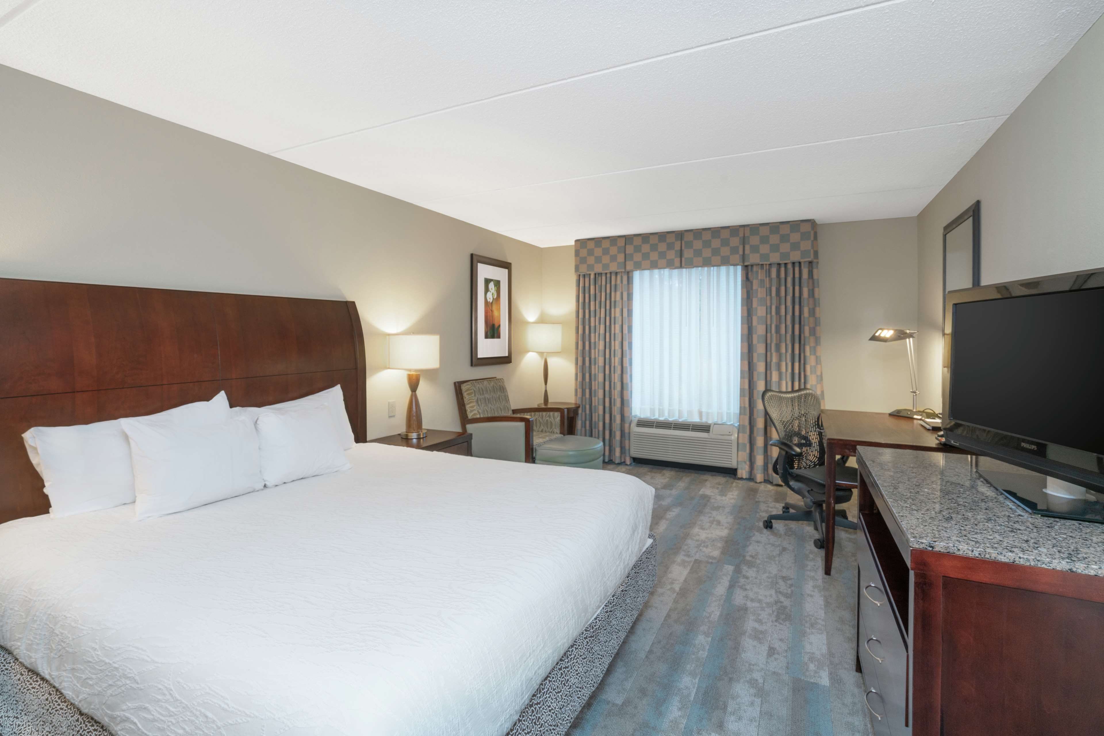 Une chambre d’hôtel avec un grand lit, un bureau avec une télévision, une chaise et une fenêtre avec des rideaux.