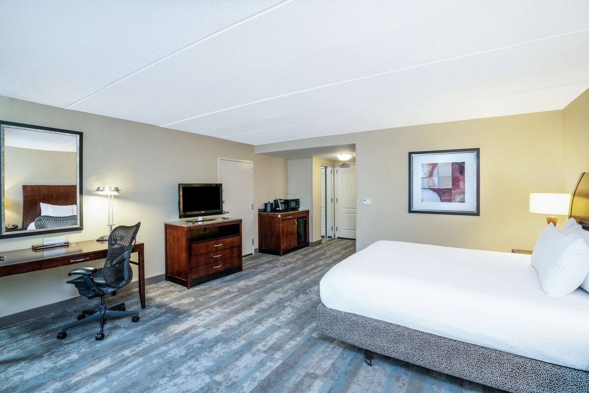 Een hotelkamer met een bed, bureau, stoel, televisie en een deur naar een andere kamer.