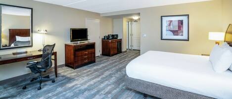 A hotel room with a bed, desk, chair, TV, and a door leading to another room.