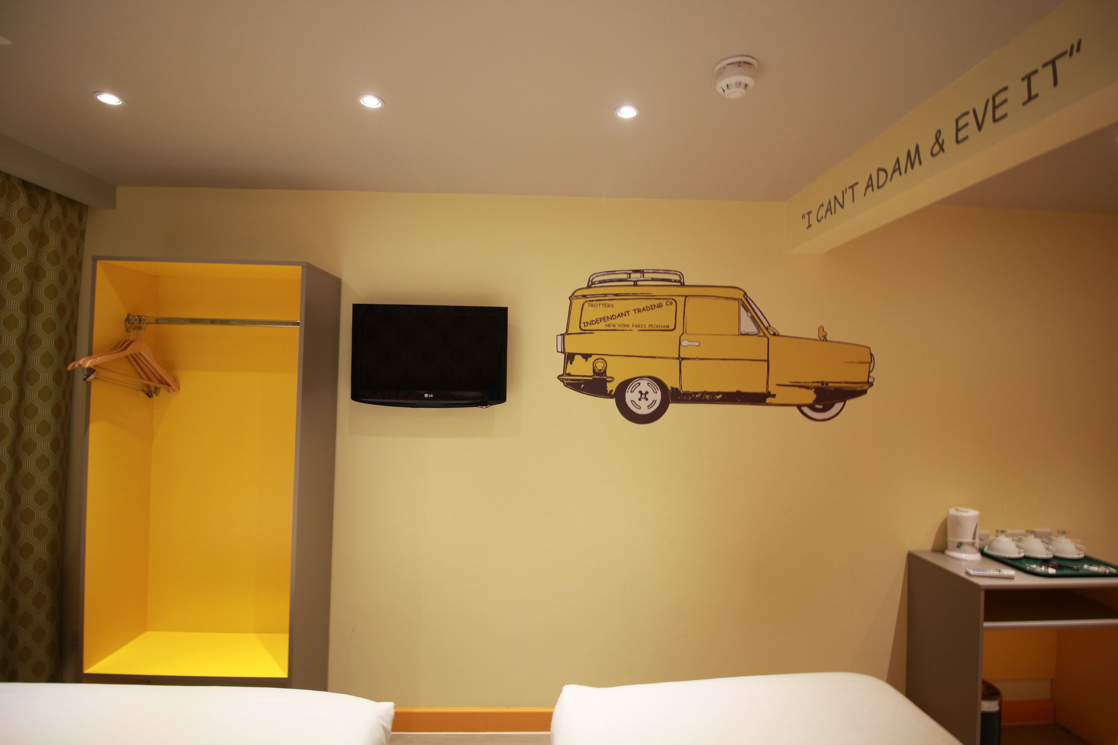 A hotel room with a bed, a shower, a television, and a wall decal of a van.