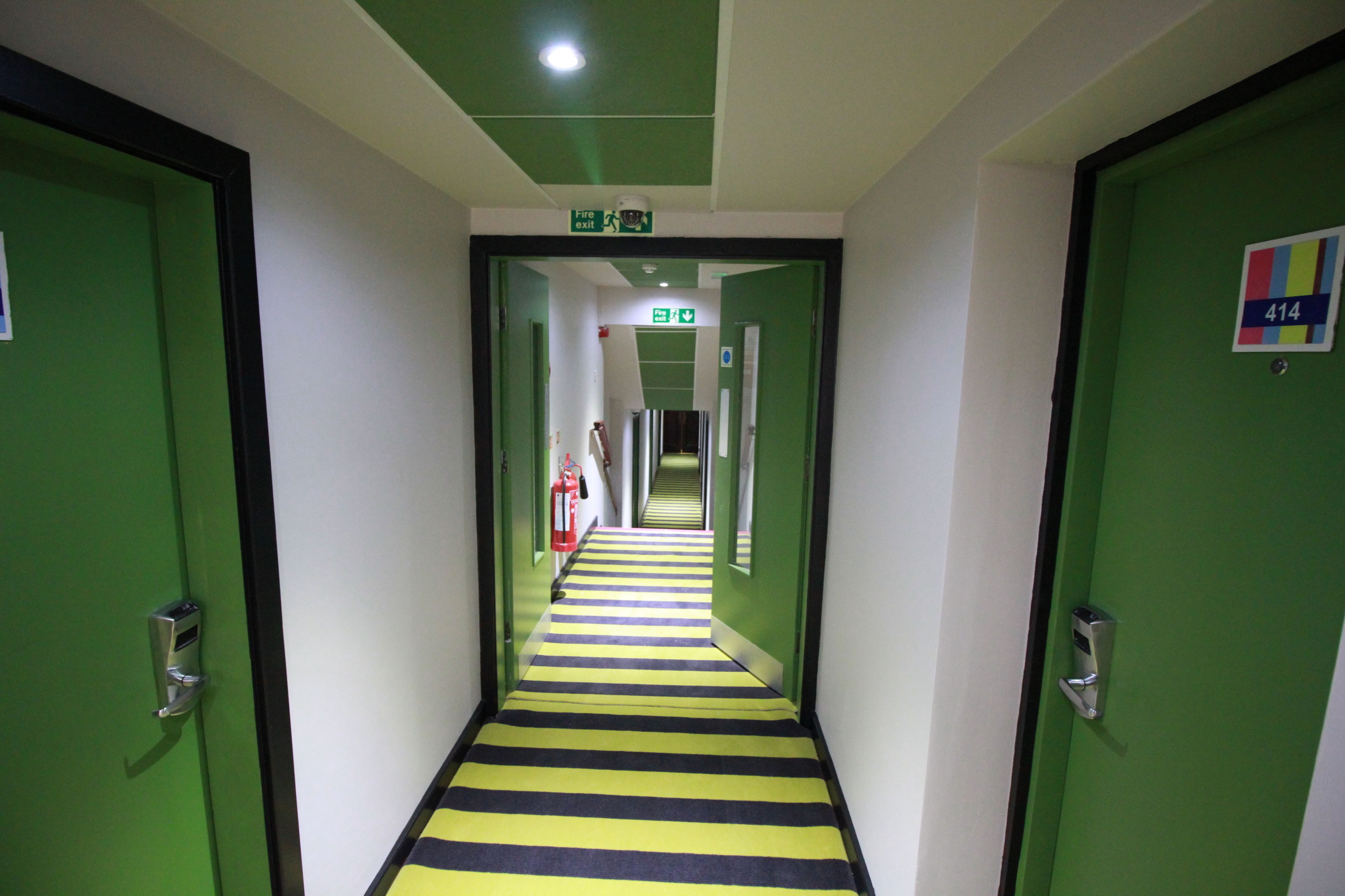 A hallway with green doors, a striped floor, and an exit sign.