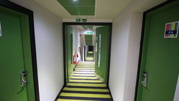 A hallway with green doors, a striped floor, and an exit sign.