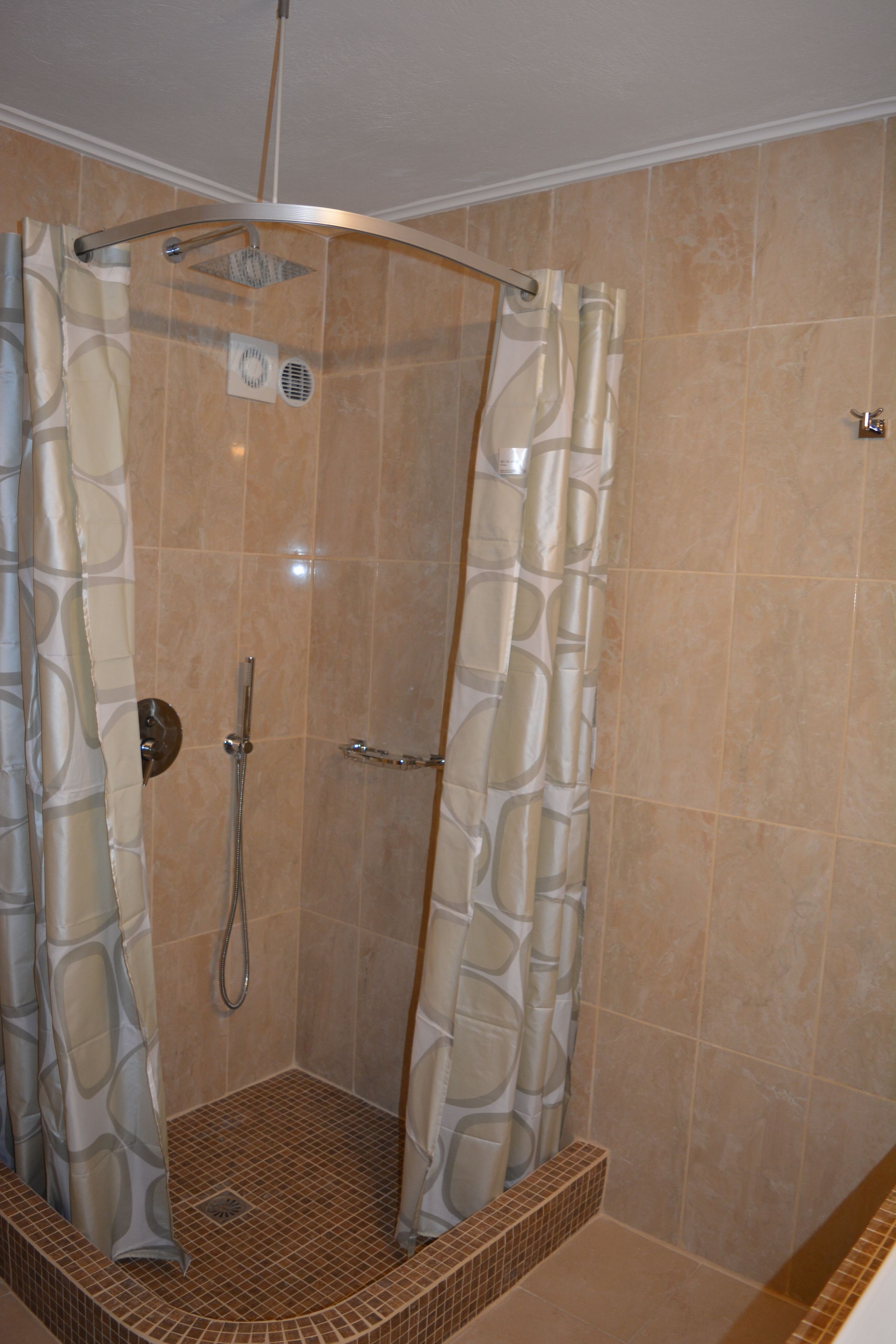 A walk-in shower with a curved glass door, a showerhead, and a small tiled floor.