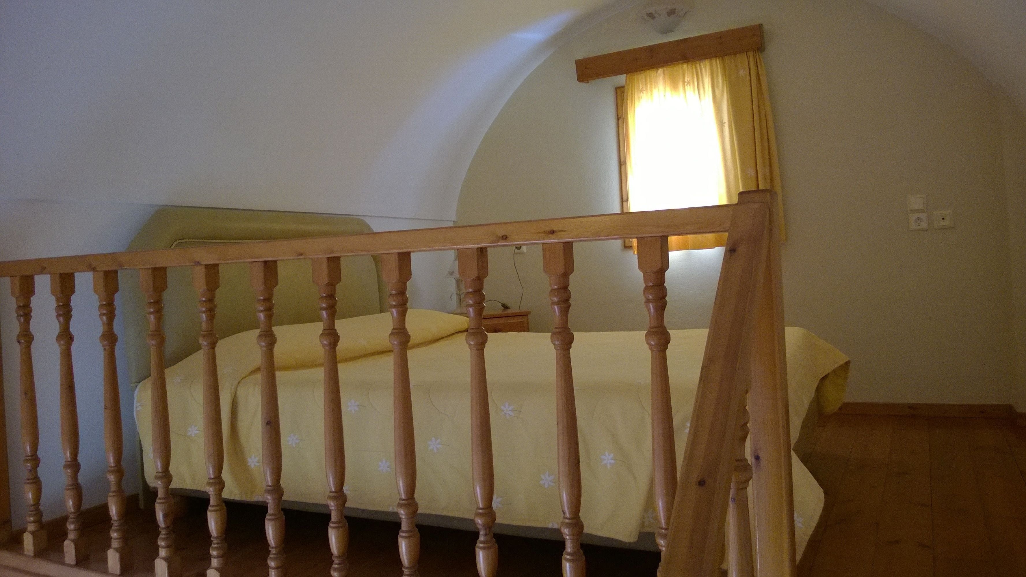 A bedroom with a wooden bed frame, a yellow bedspread, and a window with yellow curtains.