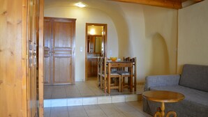 A wooden interior with a dining area, a sofa, and a kitchen visible through an open doorway. - Anemomilos Suites (Santorini)