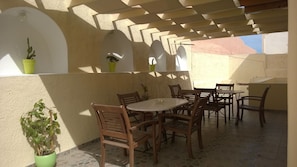 Eine Terrasse im Freien mit einem runden Tisch und Holzstühlen, umgeben von Topfpflanzen und einem gefliesten Boden.