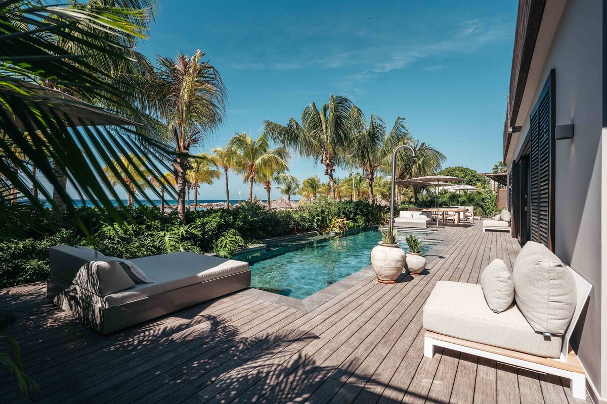 A wooden deck with a pool, lounge chairs, and palm trees.