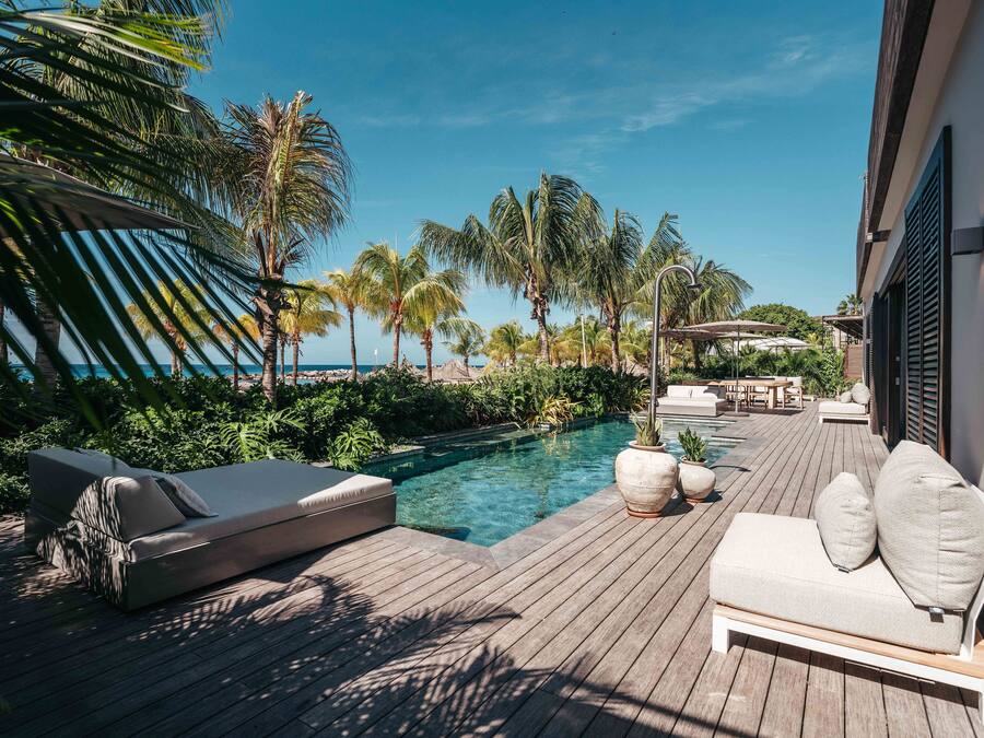 Une terrasse en bois avec une piscine, des chaises longues et des palmiers.