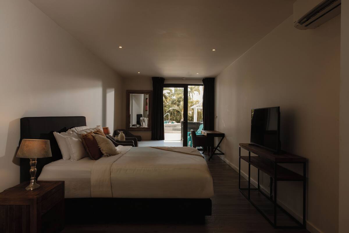 A modern hotel room with a large bed, a desk, a television, and a view of the outdoors.