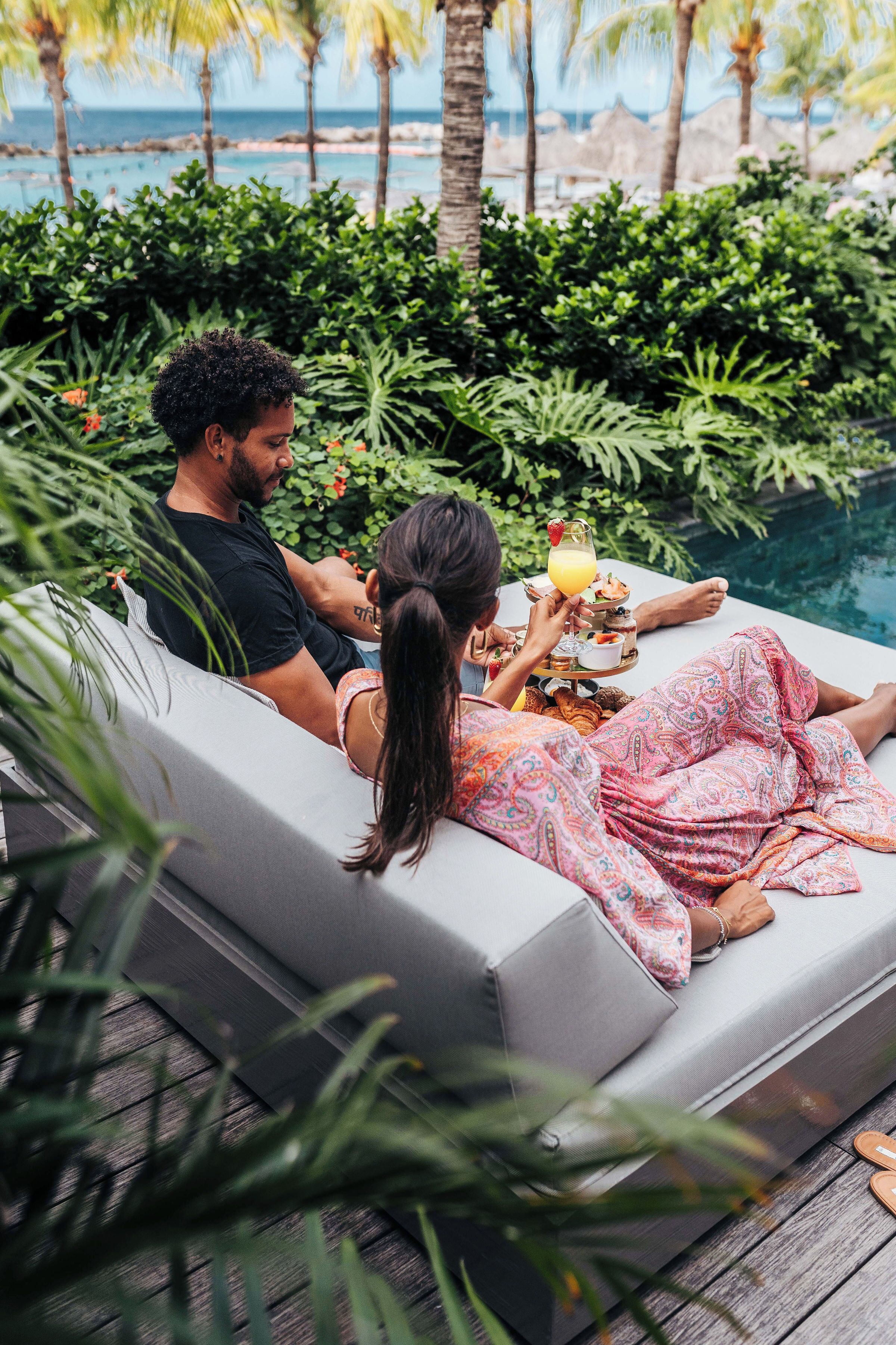 A couple relaxing by a poolside lounge with a drink tray.