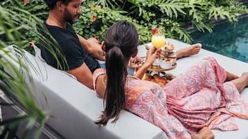 Un couple se détend au bord d’une piscine, sur des chaises longues, avec un plateau de boissons.
