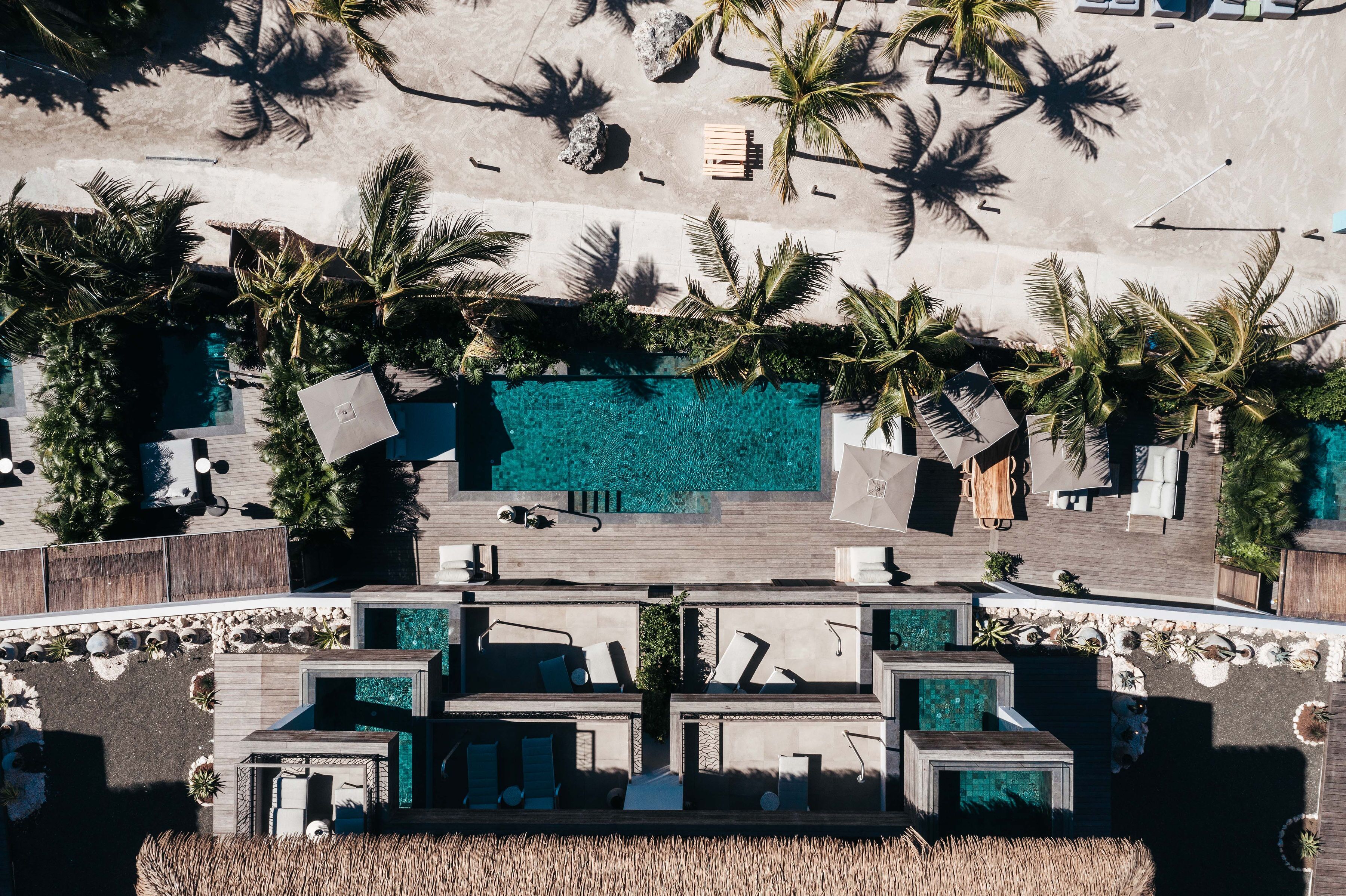 Luftaufnahme eines Resorts mit Schwimmbad, Liegebereichen und Palmen.