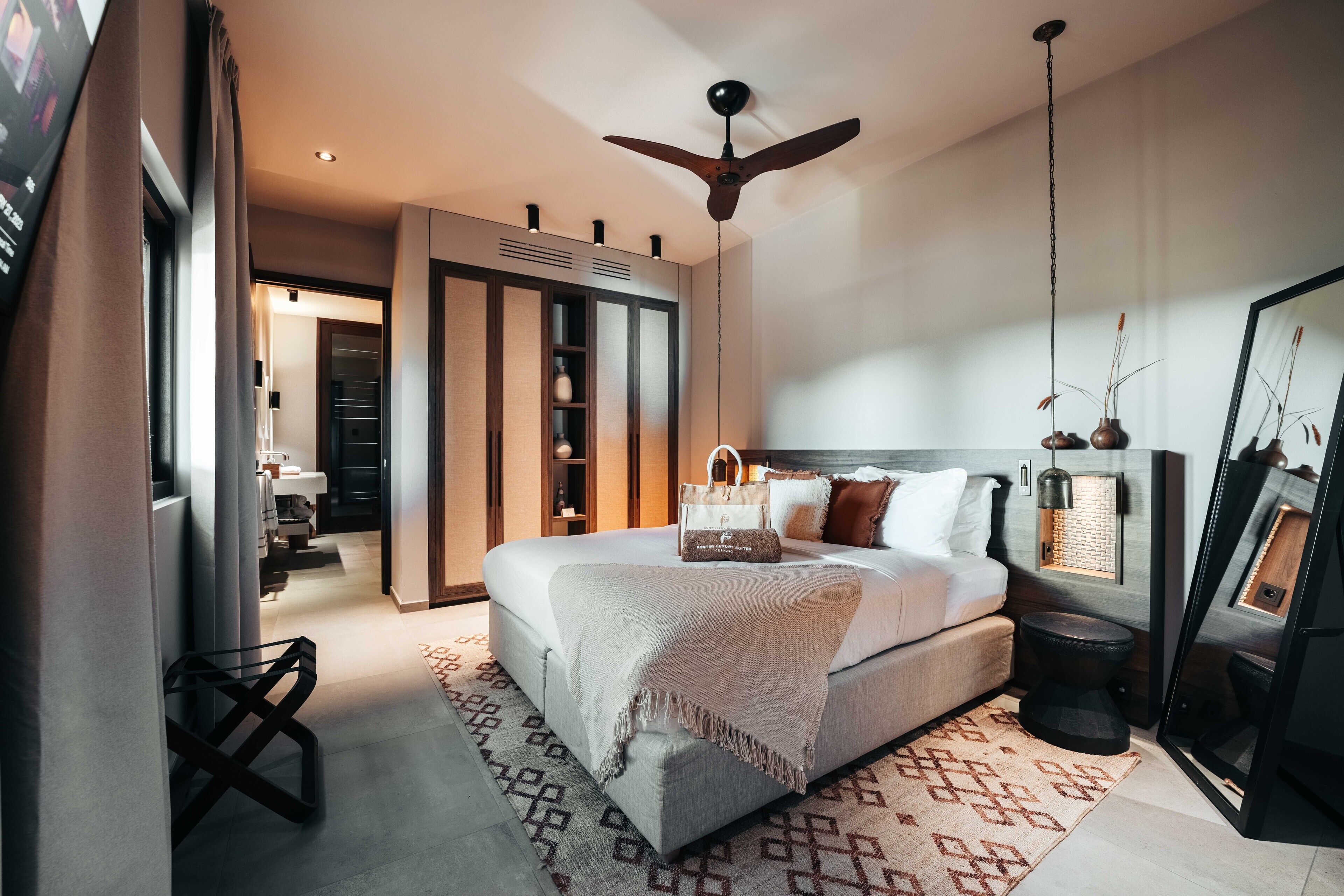Een moderne slaapkamer met een groot bed, een plafondventilator, een kledingkast en een badkamer met spiegel en handdoekrek.