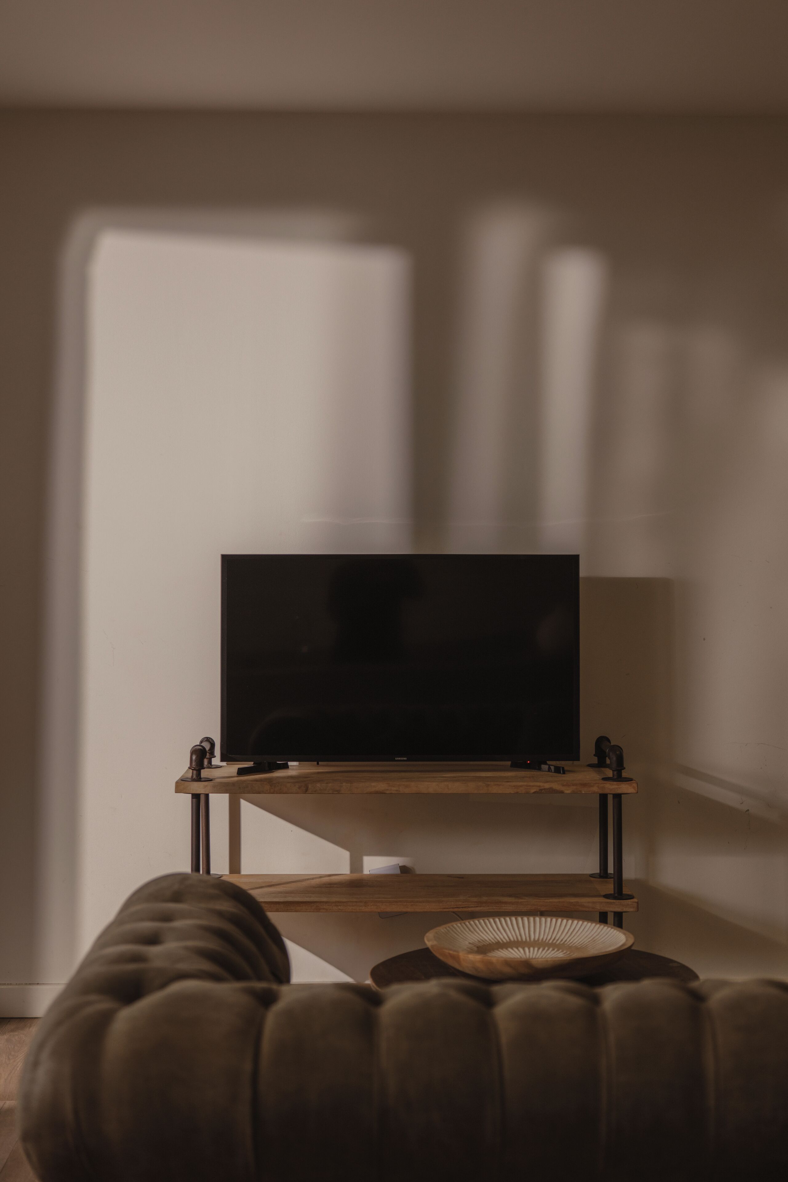 A living room with a flat-screen TV on a wooden stand, a cushioned ottoman, and a woven basket.