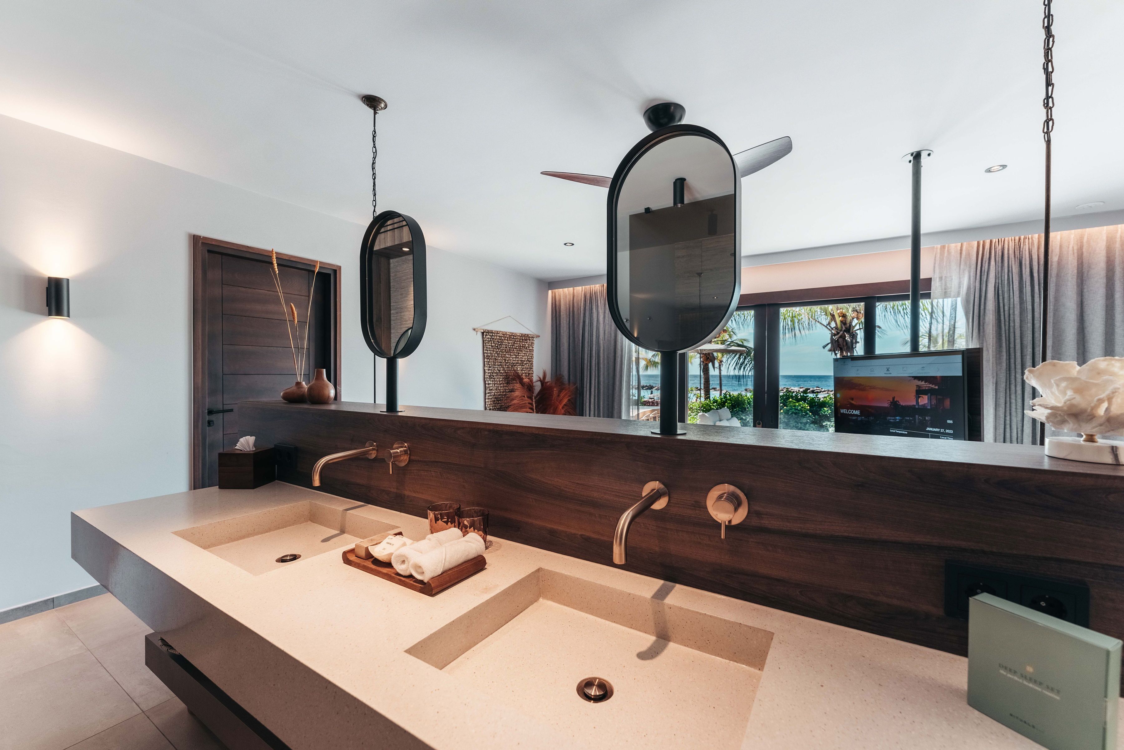 Een moderne badkamer met een groot wastafelmeubel, twee spiegels en uitzicht op de oceaan door grote ramen.
