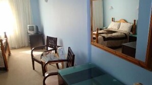 A bedroom with a bed, a chair, a desk, a mirror, and a television. - Stansted Skyline Hotel (Dunmow)