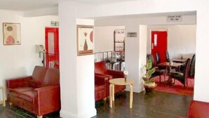 A spacious living area with a red sofa, a small round table, and a bookshelf. - Stansted Skyline Hotel (Dunmow)