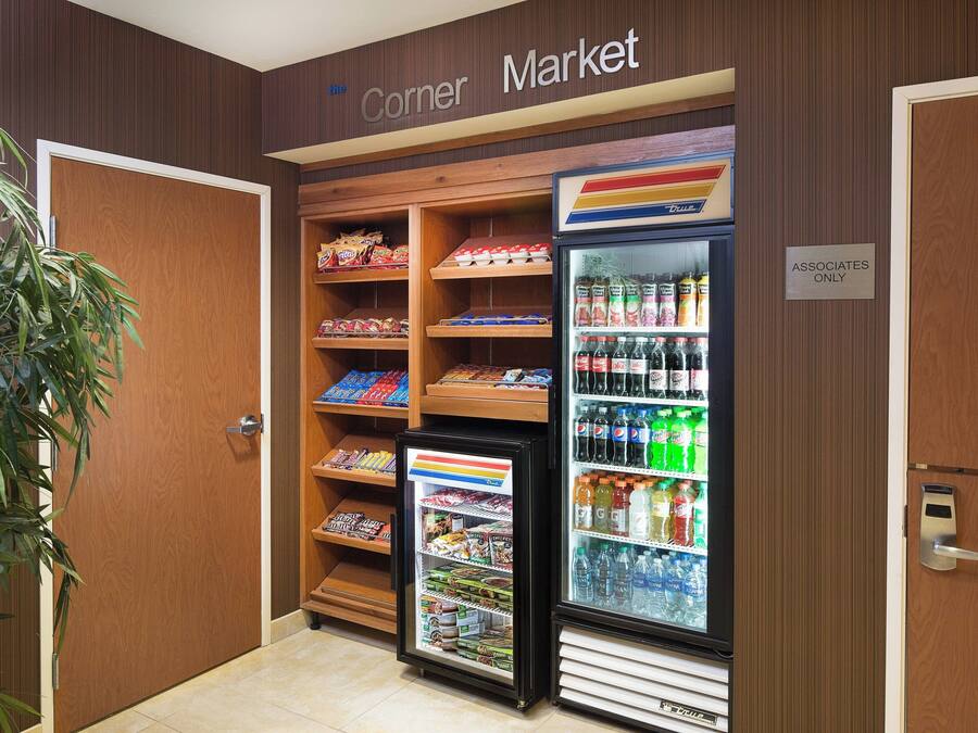 Une petite épicerie de quartier avec des étagères remplies d’en-cas et de boissons, un présentoir réfrigéré et un panneau indiquant qu’elle est réservée aux employés.