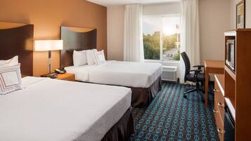 A hotel room with two beds, a desk, a chair, a lamp, and a view of the outdoors.