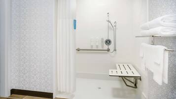 Un área de ducha moderna con puerta de vidrio, un pasamanos y un estante con toallas dobladas.
