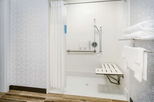 Un área de ducha moderna con puerta de vidrio, un pasamanos y un estante con toallas dobladas.