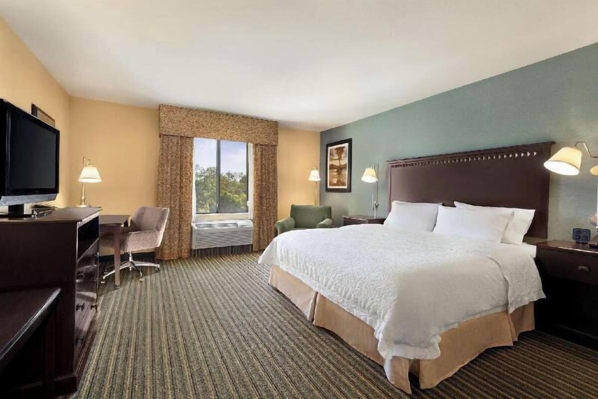 A hotel room with a bed, desk, chair, television, and a window with curtains.