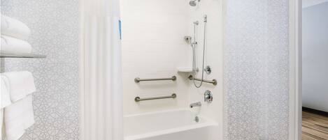 Un baño moderno con ducha, barras de apoyo y una bañera blanca.
