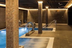 Een wellnessruimte met een zwembad, zuilen en een douchegedeelte.