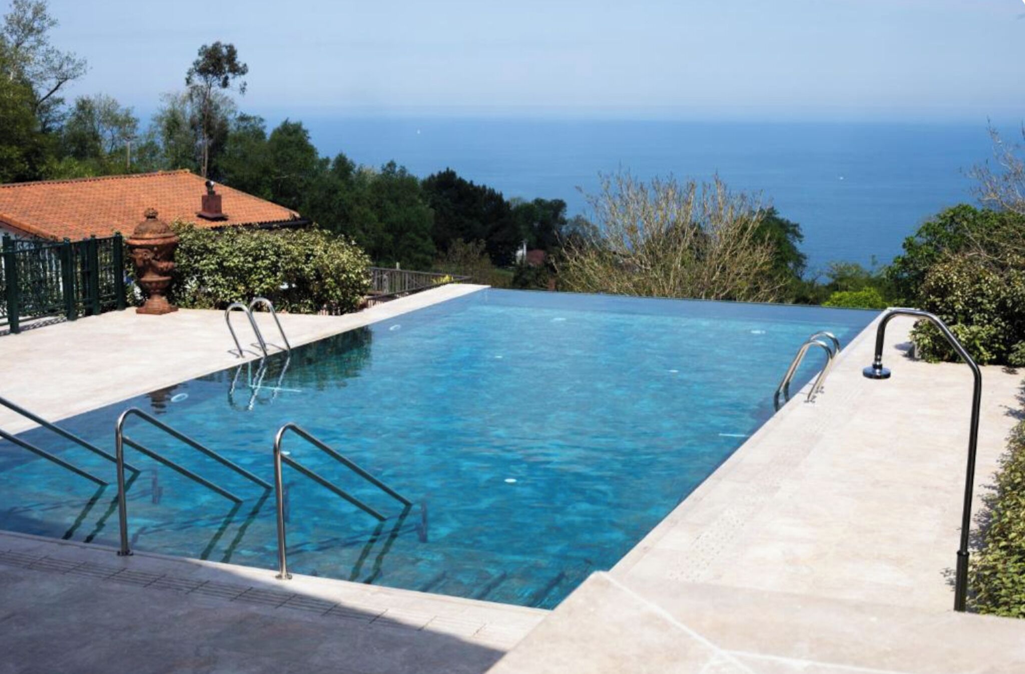A rectangular swimming pool with clear blue water, surrounded by a paved deck and metal railings.